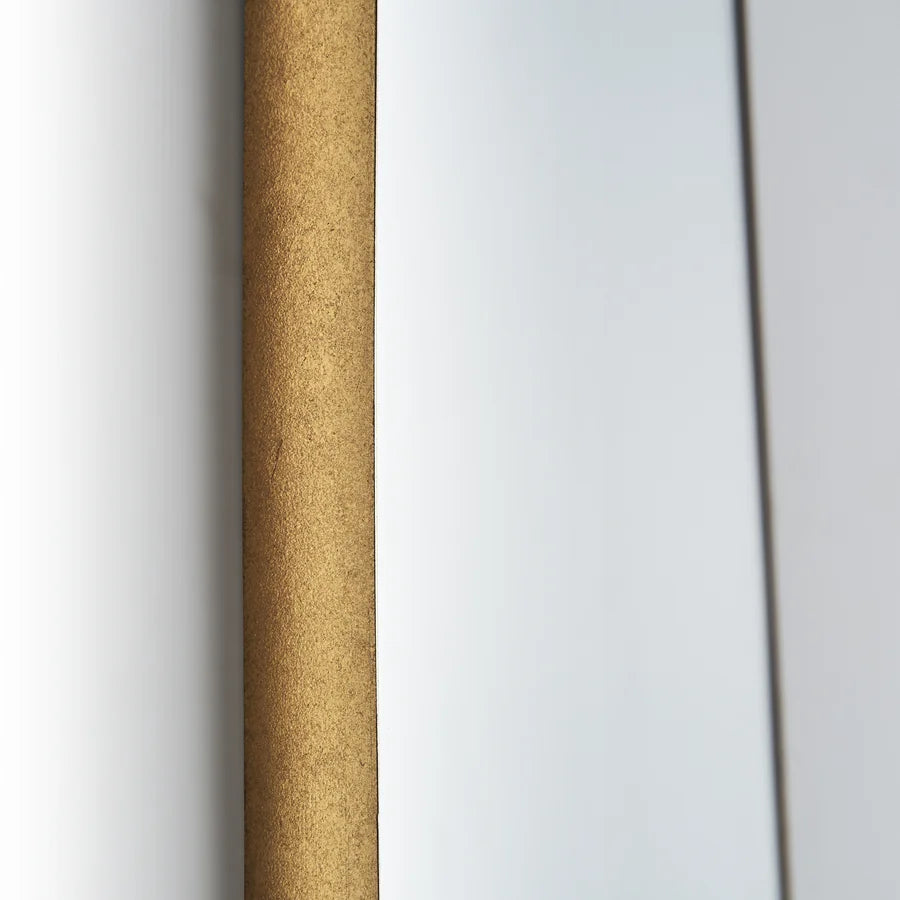 Primer plano del canto del marco del Espejo Bera, de textura dorada mate, contra la pared