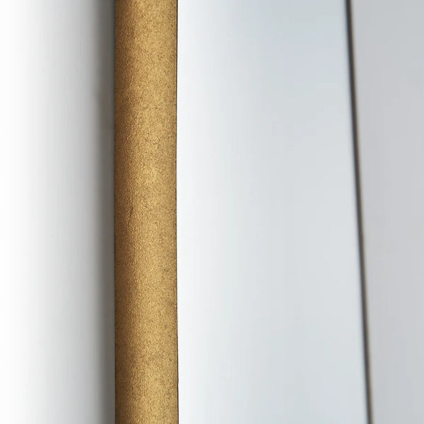 Primer plano del canto del marco del Espejo Bera, de textura dorada mate, contra la pared