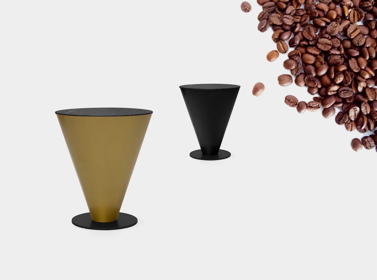 Dos mesas Peonza 01, una dorada y otra en el metal negro de serie, en una composición con granos de café