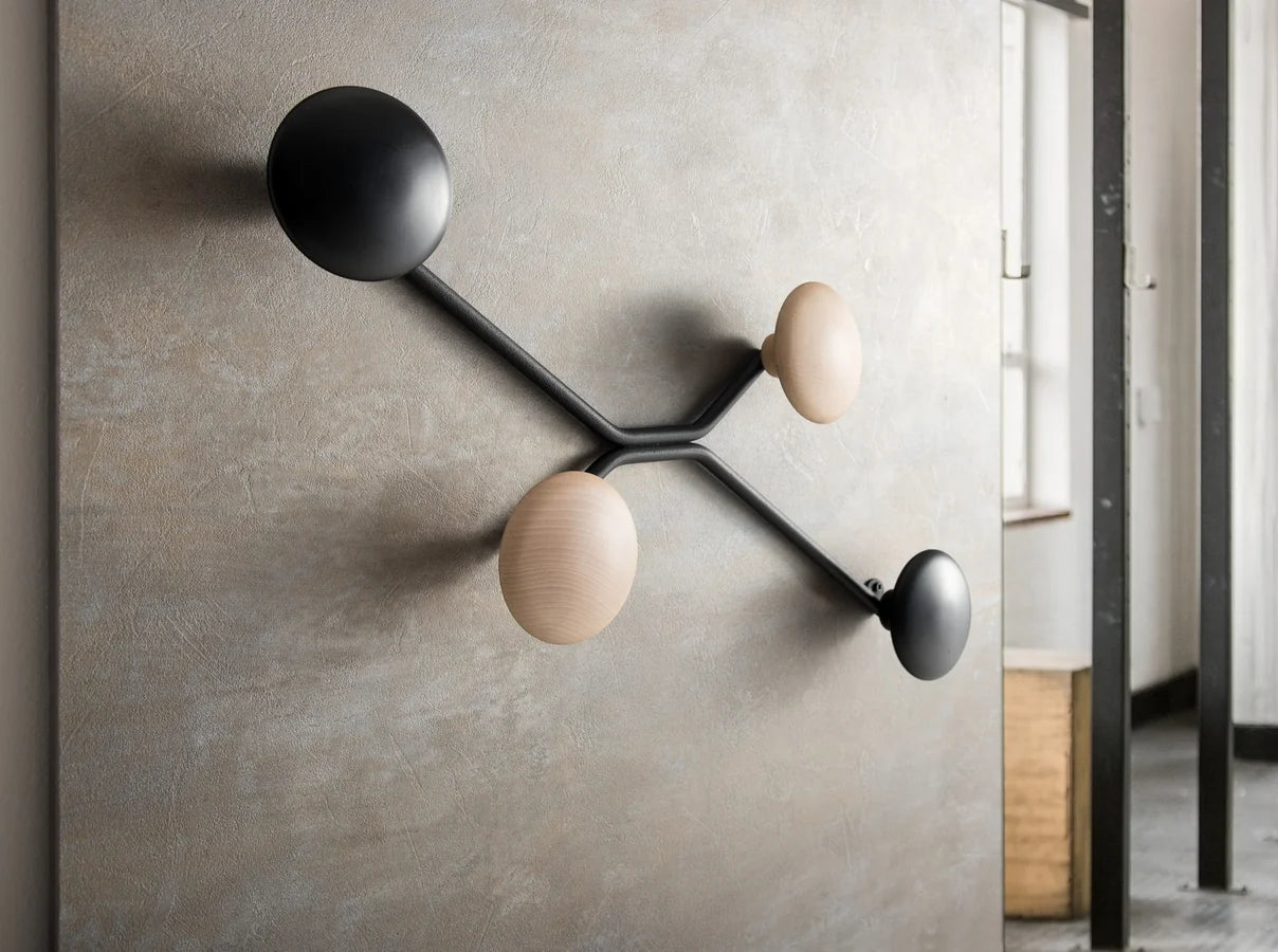 Perchero de pared Spyder montado sobre un muro de microcemento, con dos prendas colgadas