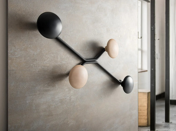 Perchero de pared Spyder montado sobre un muro de microcemento, con dos prendas colgadas