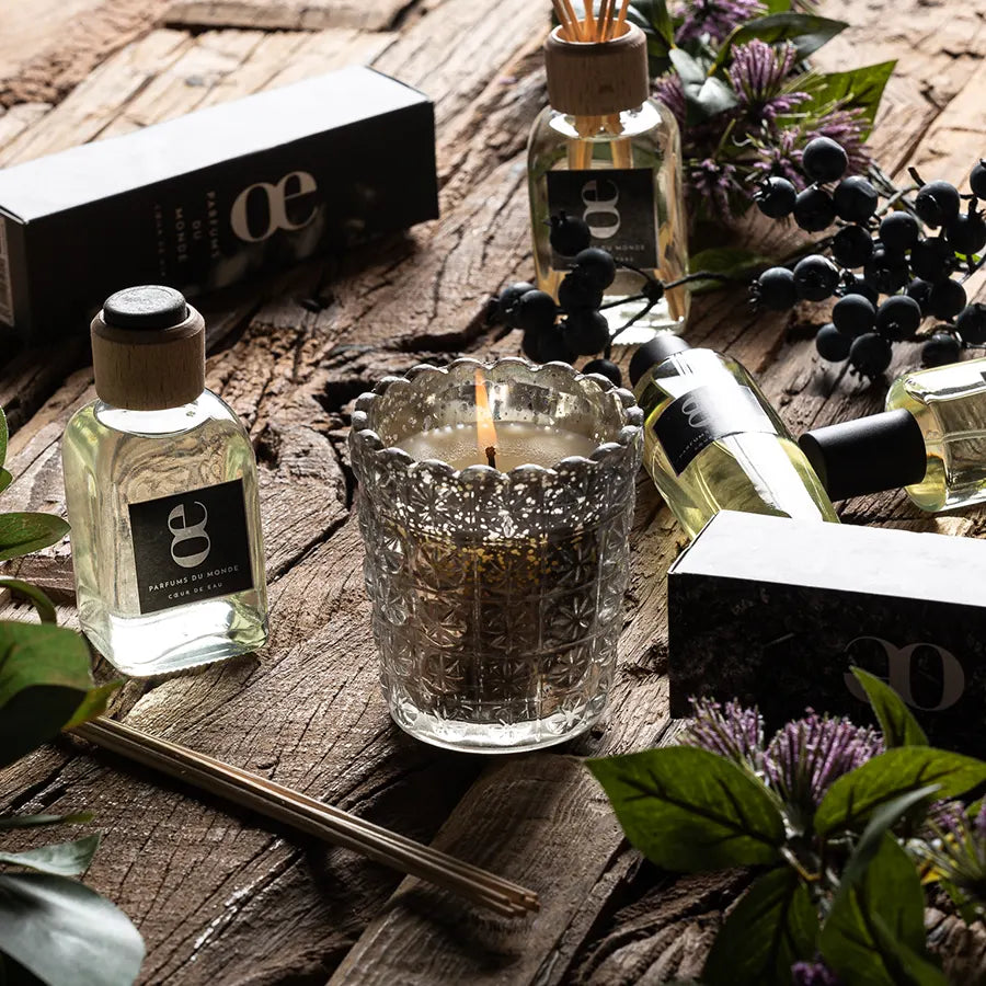 Vela Tierra encendida sobre una mesa de madera, entre los perfumes y difusores de la gama